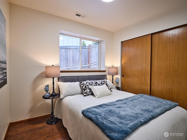 bedroom with dark wood-style floors, baseboards, visible vents, and a closet