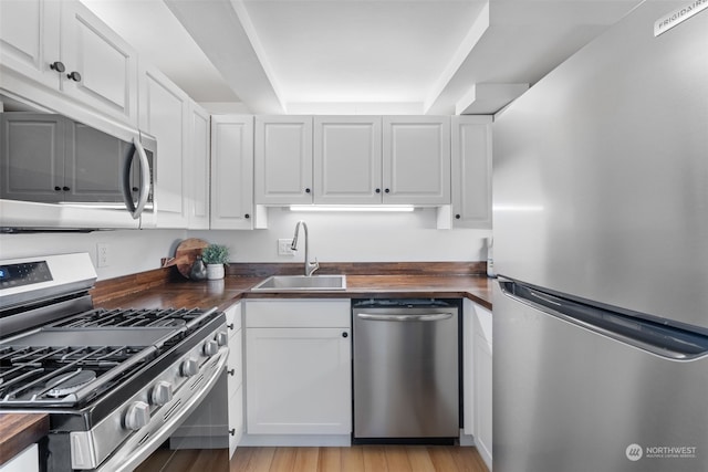 kitchen featuring butcher block counters, sink, appliances with stainless steel finishes, light hardwood / wood-style floors, and white cabinetry