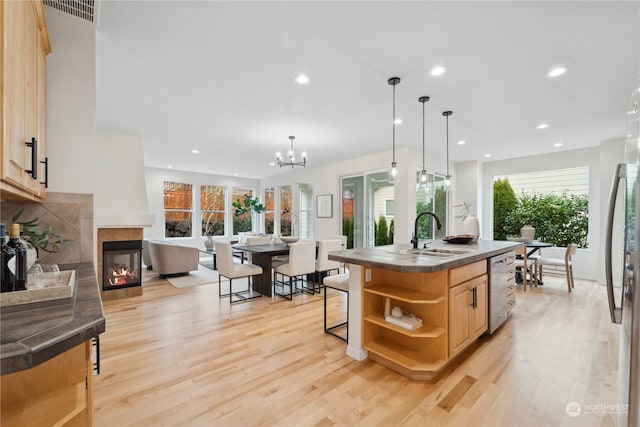 kitchen featuring a kitchen island with sink, appliances with stainless steel finishes, hanging light fixtures, a multi sided fireplace, and light brown cabinetry