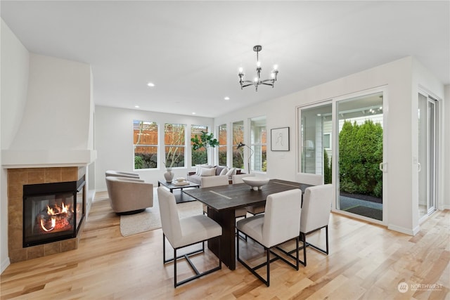 dining space featuring a tile fireplace, a chandelier, and light hardwood / wood-style floors