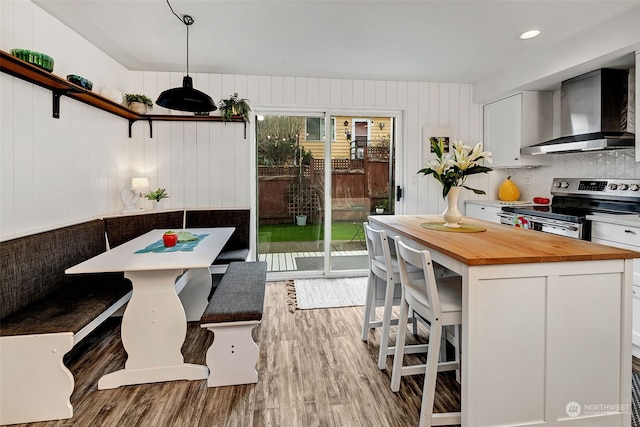 kitchen featuring wall chimney exhaust hood, stainless steel electric range, plenty of natural light, white cabinets, and a breakfast bar area