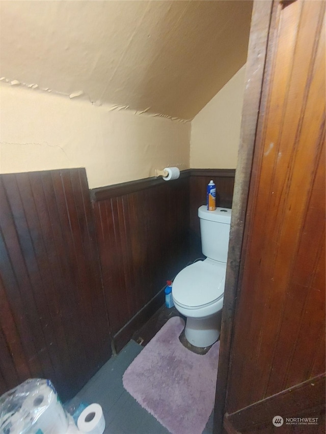 bathroom featuring toilet, wood walls, and lofted ceiling