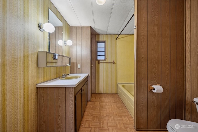 bathroom with wooden walls, a bath, toilet, parquet floors, and vanity