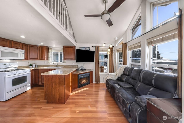 kitchen with white appliances, a high ceiling, light wood-style floors, open floor plan, and brown cabinets