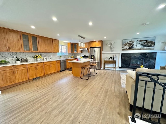 kitchen featuring light hardwood / wood-style floors, a breakfast bar area, appliances with stainless steel finishes, a fireplace, and a kitchen island