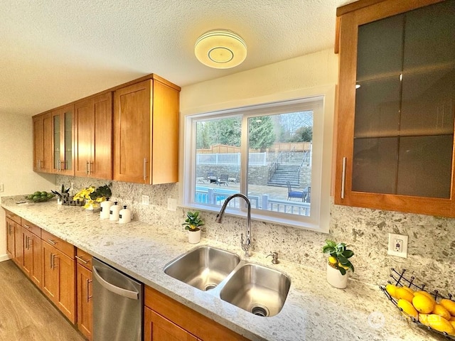 kitchen with tasteful backsplash, dishwasher, sink, light wood-type flooring, and light stone counters