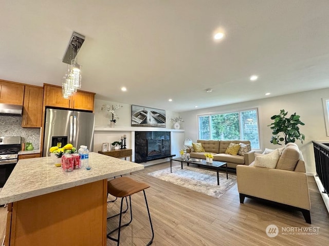 kitchen with exhaust hood, stainless steel appliances, a kitchen breakfast bar, backsplash, and a tile fireplace