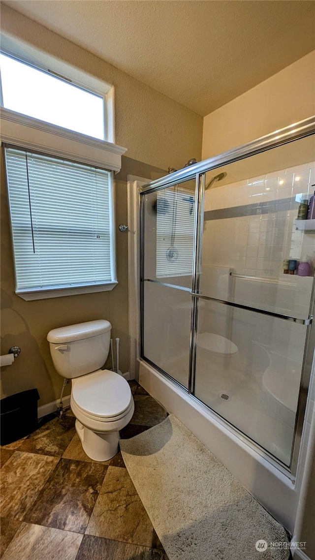 bathroom featuring a textured ceiling, a shower with door, and toilet