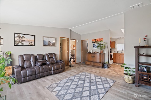 living room featuring lofted ceiling, light wood-type flooring, and sink