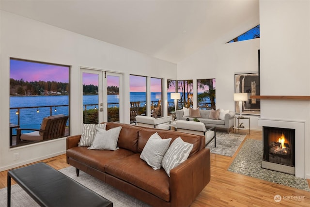 living room with french doors, high vaulted ceiling, light wood-type flooring, and a water view