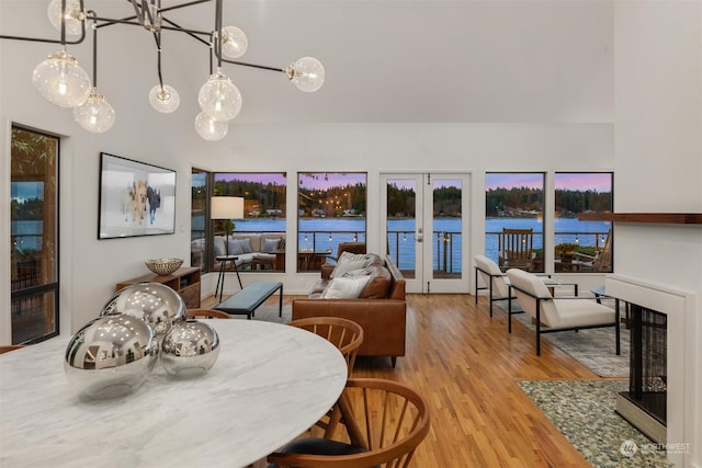 dining room with french doors, light hardwood / wood-style flooring, a multi sided fireplace, and a water view