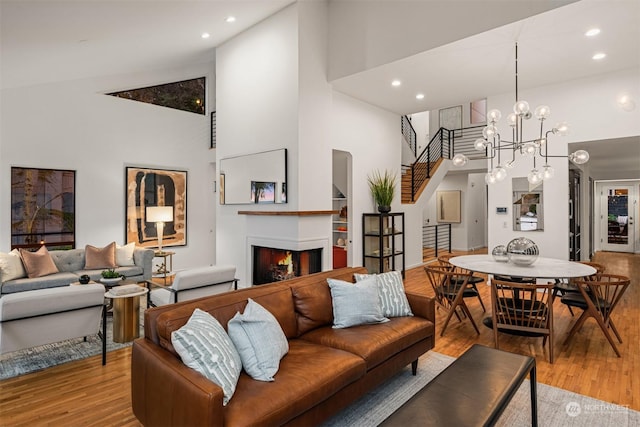 living room featuring high vaulted ceiling, built in features, light hardwood / wood-style floors, and a chandelier