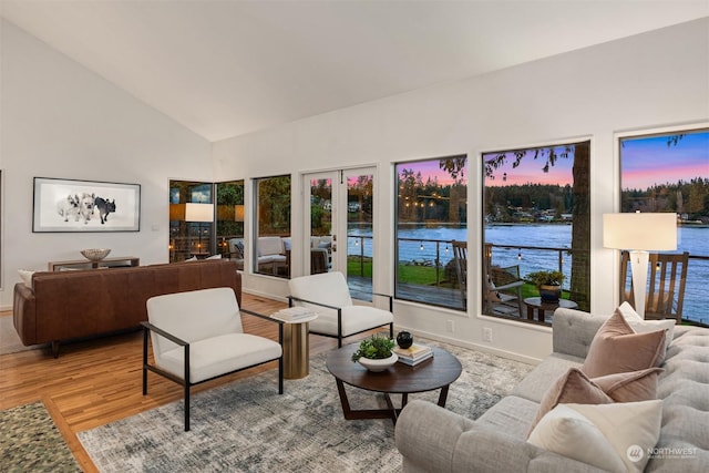 living room featuring french doors, high vaulted ceiling, light hardwood / wood-style floors, and a water view