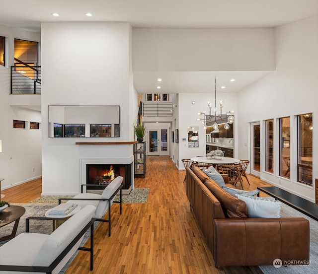 living room with light wood-type flooring, an inviting chandelier, and a towering ceiling