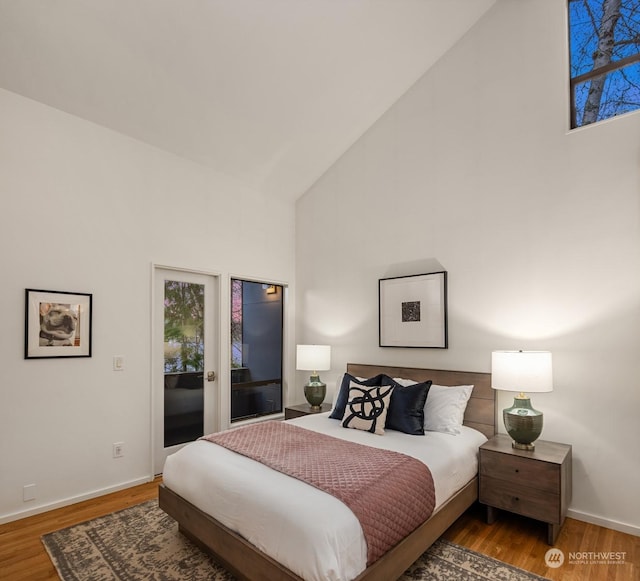 bedroom with access to outside, high vaulted ceiling, and wood-type flooring