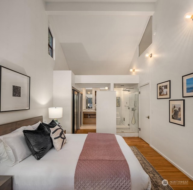 bedroom with high vaulted ceiling, beam ceiling, light hardwood / wood-style flooring, and connected bathroom