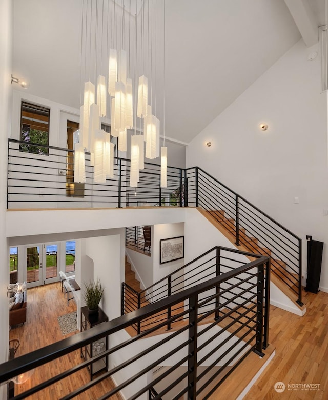 staircase featuring a towering ceiling, beamed ceiling, hardwood / wood-style flooring, and a notable chandelier