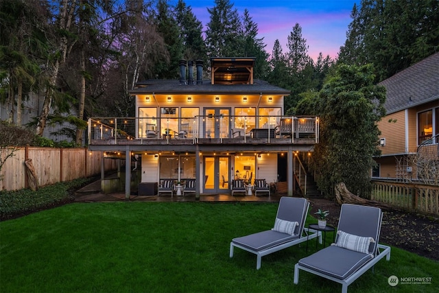 back house at dusk with a lawn, a patio, a balcony, and a wooden deck