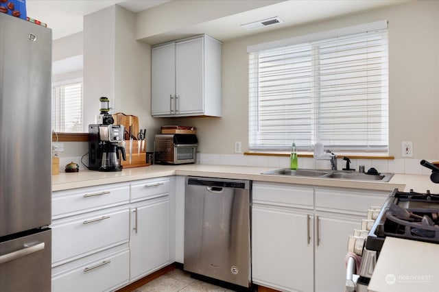 kitchen with appliances with stainless steel finishes, white cabinetry, sink, and light tile patterned floors