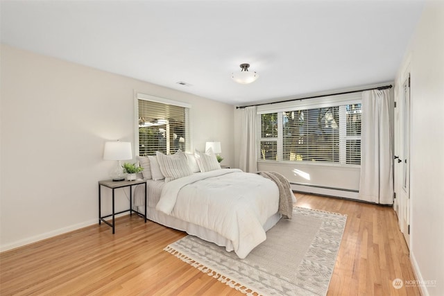 bedroom featuring a baseboard radiator, hardwood / wood-style floors, and multiple windows