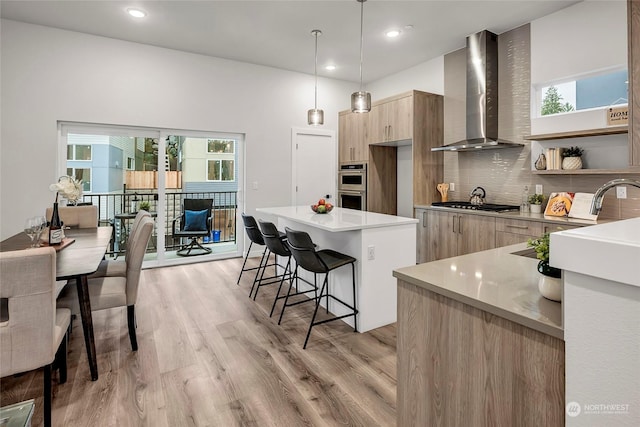 kitchen with pendant lighting, backsplash, a center island, light hardwood / wood-style floors, and wall chimney exhaust hood