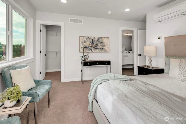 bedroom featuring an AC wall unit, a spacious closet, light carpet, ensuite bath, and a closet