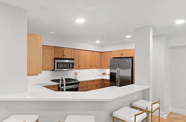 kitchen with tasteful backsplash, appliances with stainless steel finishes, a breakfast bar, and kitchen peninsula