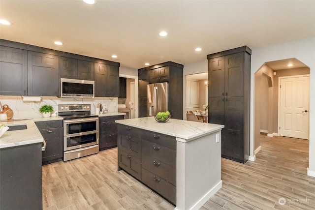 kitchen featuring appliances with stainless steel finishes, light wood-type flooring, a center island, light stone counters, and tasteful backsplash