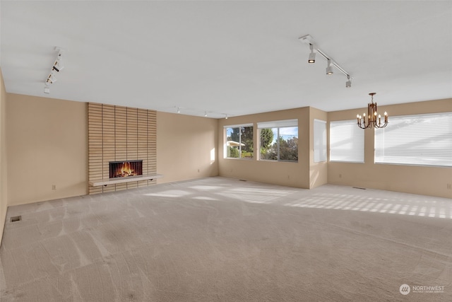 unfurnished living room with a fireplace, light colored carpet, rail lighting, and a chandelier