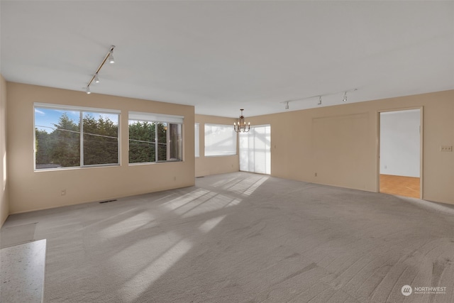 spare room with a notable chandelier, track lighting, and light carpet