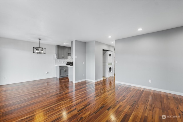 unfurnished living room with dark wood-type flooring, stacked washer and clothes dryer, and a notable chandelier