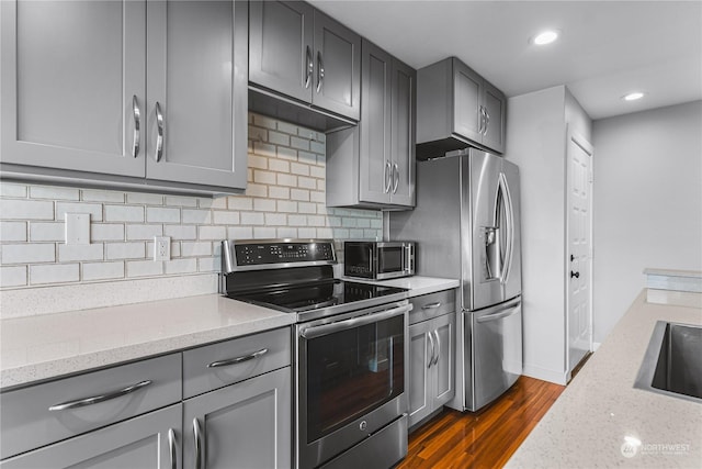 kitchen with light stone counters, dark hardwood / wood-style floors, gray cabinetry, and stainless steel appliances