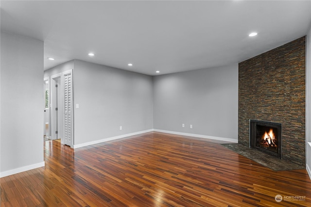 unfurnished living room featuring a stone fireplace and dark hardwood / wood-style flooring