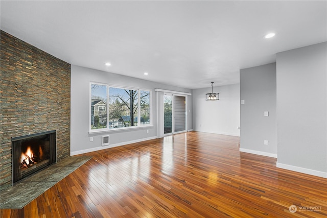 unfurnished living room featuring hardwood / wood-style flooring, a stone fireplace, and an inviting chandelier