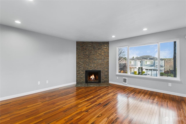 unfurnished living room with hardwood / wood-style flooring and a stone fireplace