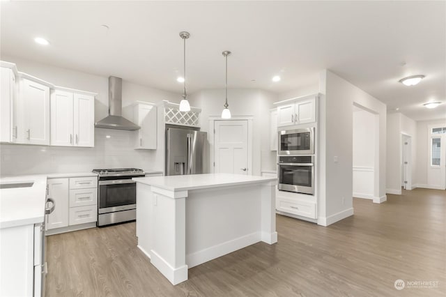 kitchen featuring decorative light fixtures, white cabinetry, decorative backsplash, stainless steel appliances, and wall chimney range hood