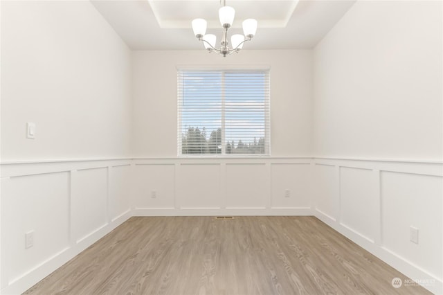 unfurnished room featuring an inviting chandelier, a tray ceiling, and light hardwood / wood-style floors