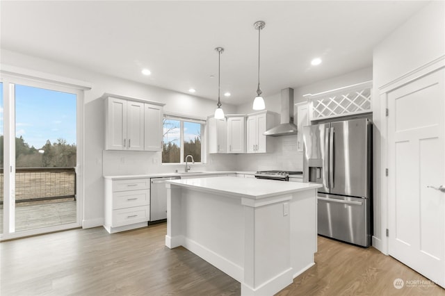 kitchen featuring wall chimney range hood, appliances with stainless steel finishes, hanging light fixtures, white cabinets, and a kitchen island