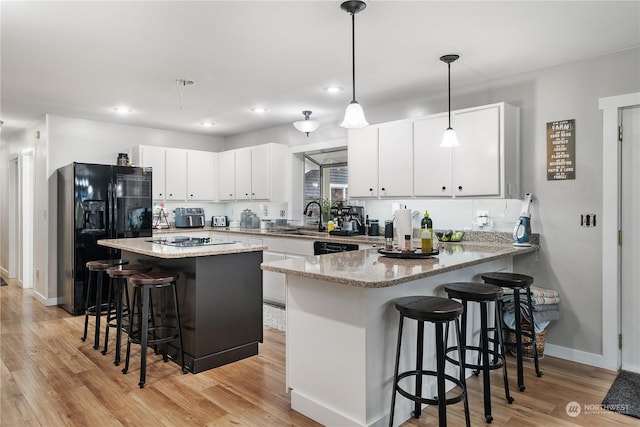 kitchen featuring white cabinetry, black refrigerator with ice dispenser, pendant lighting, kitchen peninsula, and a breakfast bar