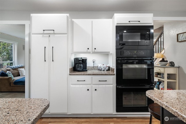 kitchen featuring light stone countertops, light wood-type flooring, black appliances, and white cabinetry