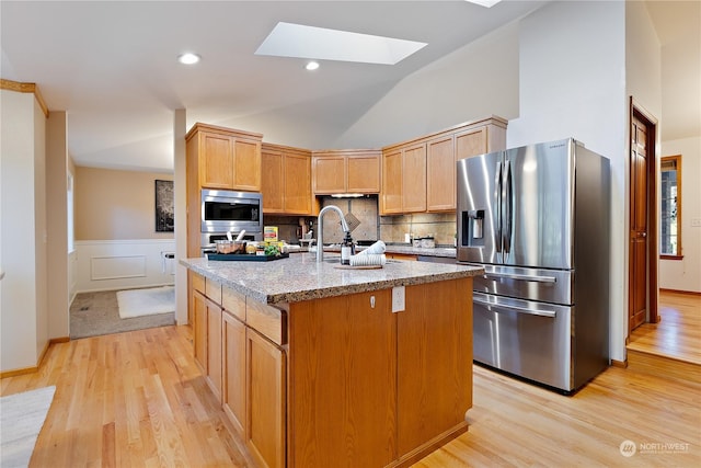 kitchen featuring tasteful backsplash, sink, stainless steel appliances, light stone countertops, and a center island with sink