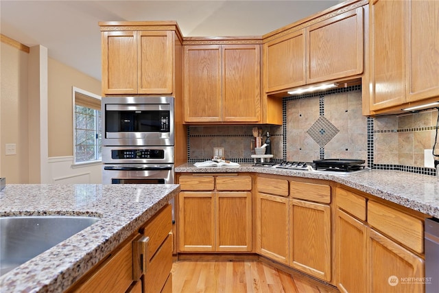 kitchen featuring appliances with stainless steel finishes, decorative backsplash, light stone counters, and light hardwood / wood-style flooring