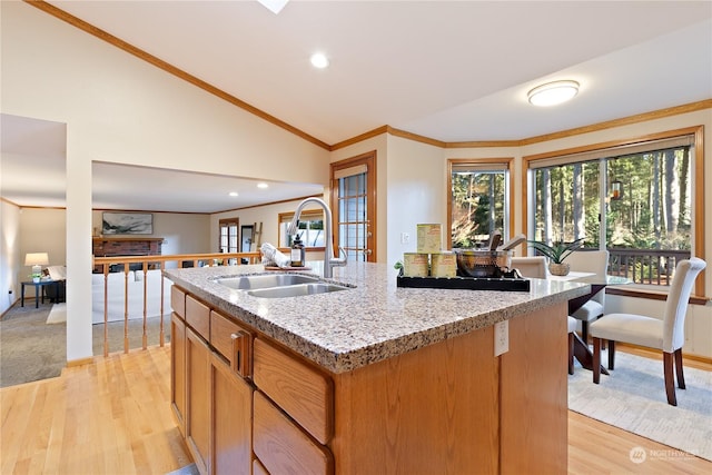 kitchen featuring lofted ceiling, sink, light hardwood / wood-style flooring, ornamental molding, and an island with sink