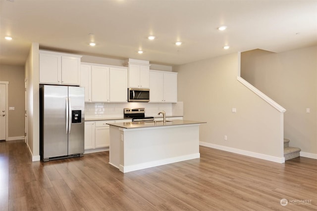 kitchen featuring stainless steel appliances, white cabinets, a center island with sink, decorative backsplash, and light wood-type flooring