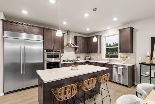 kitchen featuring appliances with stainless steel finishes, a kitchen island, wall chimney exhaust hood, sink, and decorative light fixtures