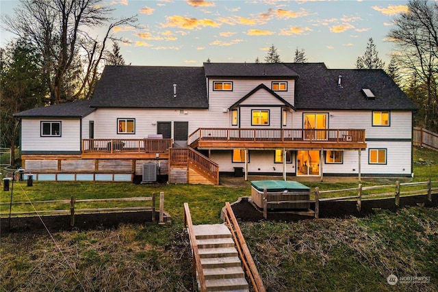 back house at dusk with cooling unit, a deck, and a lawn