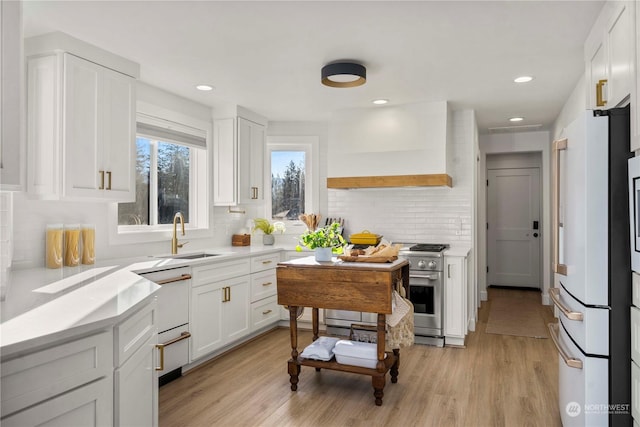 kitchen featuring high quality appliances, white cabinetry, sink, light hardwood / wood-style floors, and custom range hood