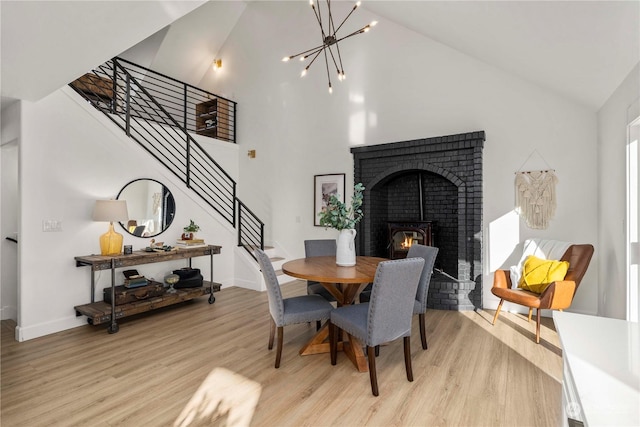 dining area featuring an inviting chandelier, high vaulted ceiling, a fireplace, and light hardwood / wood-style floors