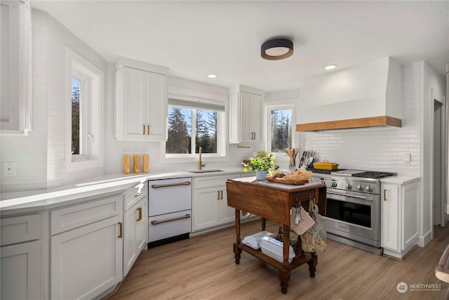 kitchen with sink, high end stainless steel range oven, white cabinetry, light hardwood / wood-style floors, and custom range hood