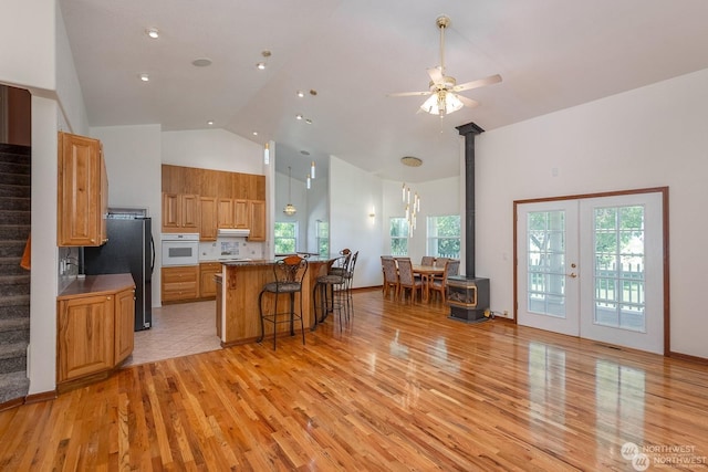 kitchen with a wood stove, ceiling fan, light hardwood / wood-style flooring, high vaulted ceiling, and black refrigerator